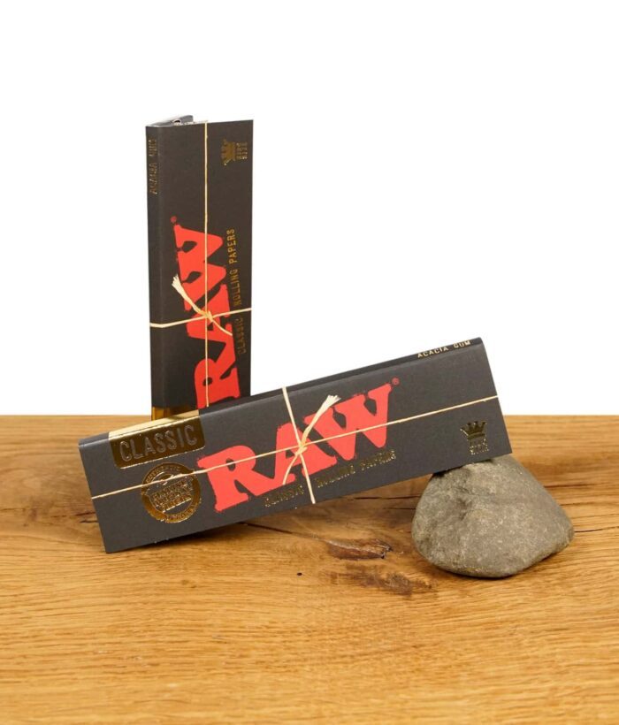 Zwei Packungen RAW Black King Size Papers auf einem Stein. Hochwertige, ungebleichte Blättchen für puren Geschmack.