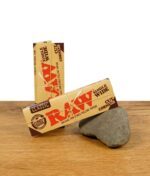 Zwei Packungen RAW Classic Rolling Papers im Single Wide Format mit Cut Corners, auf einem Stein präsentiert