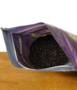 Geöffnete Verpackung einer veganen Kokosaktivkohle mit sichtbarer Kohle in Granulatform.