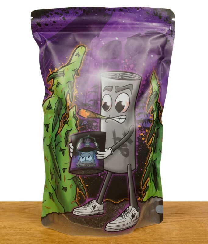 Bunte Verpackung einer veganen Kokosaktivkohle mit Cartoon-Design, das einen rauchenden Joint darstellt, der eine Tüte Kohle hält, vor einer Landschaft mit Cannabispflanzen.