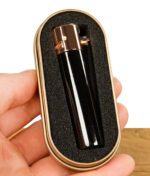 Schwarzes Clipper-Feuerzeug mit kupferner Kappe in einer gepolsterten goldenen Clipper-Metallbox, die in der Hand gehalten wird