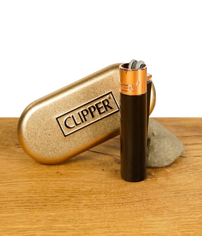 Schwarzes Clipper-Feuerzeug mit kupferner Kappe, vor einer goldenen Clipper-Metallbox platziert