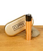 Kupferfarbenes Clipper-Feuerzeug mit schwarzer Kappe, vor einer goldenen Clipper-Metallbox stehend