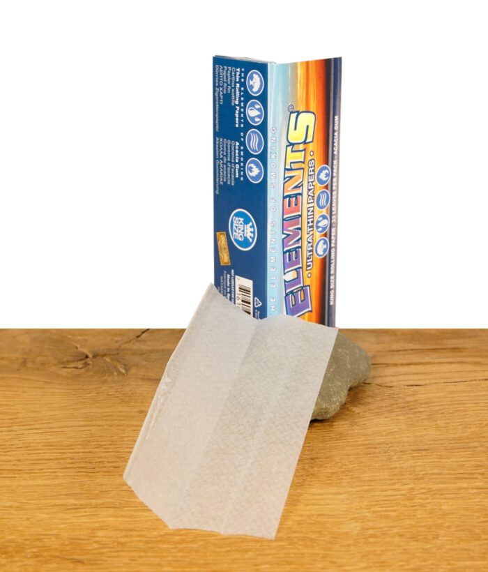 Eine geöffnete Packung Elements King Size Ultra Thin Papers auf einem Holztisch, ein einzelnes ultra dünnes Reispapier liegt vorne.