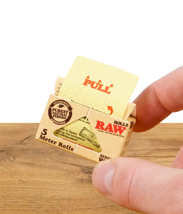 Hand hält RAW Classic Rolls Single Wide Zigarettenpapierpackung, zeigt Ziehanweisung.