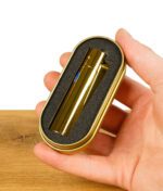 Goldenes Metal Feuerzeug in einer Schutzhülle aus Schaumstoff in einer Metallbox, gehalten von einer Hand.