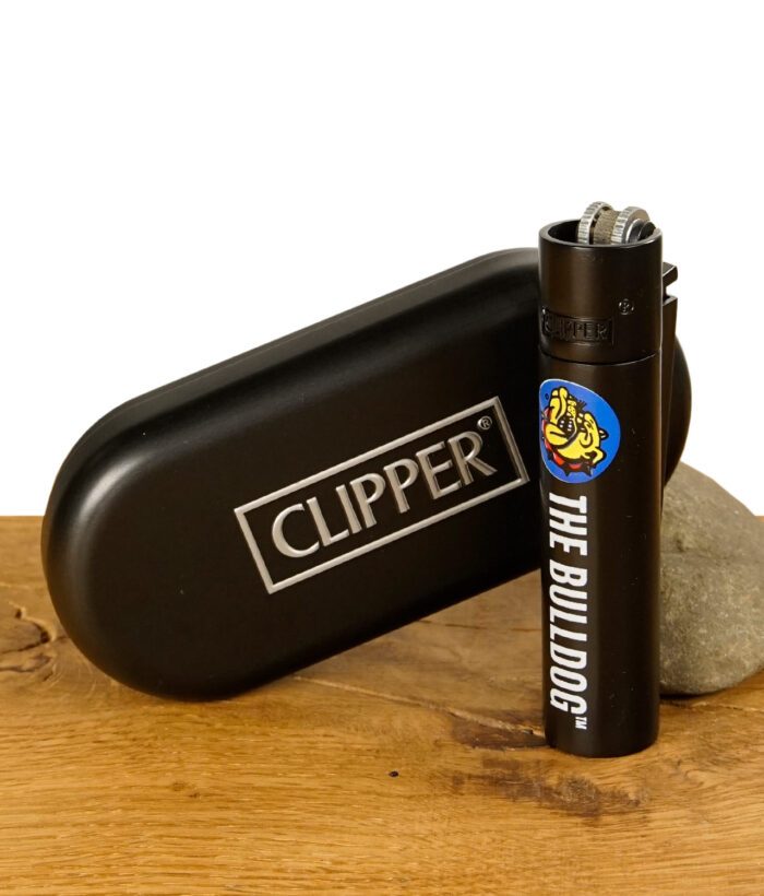 Schwarzes Clipper Metal Feuerzeug mit The Bulldog Logo neben einer schwarzen Clipper Metallbox auf Holzuntergrund.