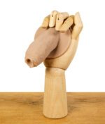 Holzmodell einer Hand, die einen ScreenyWeeny 6.0 Fake-Penis in Hautfarbe hält, auf einem Holztisch.