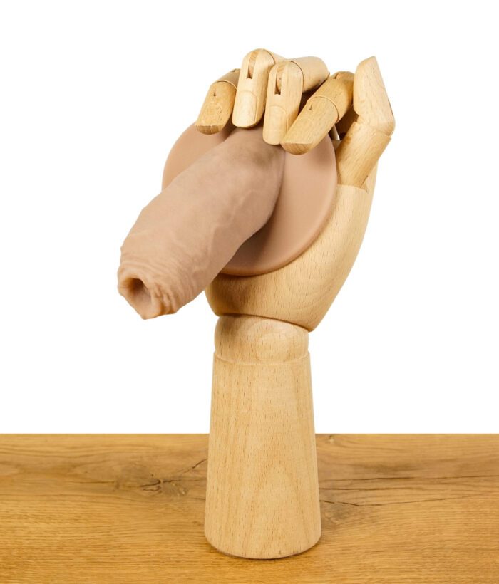 Holzmodell einer Hand, die einen ScreenyWeeny 6.0 Fake-Penis in Hautfarbe hält, auf einem Holztisch.