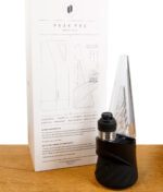 Puffco New Peak Pro mit 3DXL Kammer steht neben seiner Verpackung auf einem Holzbrett vor weißem Hintergrund