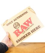 RAW Store Sign Pappschild auf Holzbrett vor weißem Hintergrund von einer Hand gehalten
