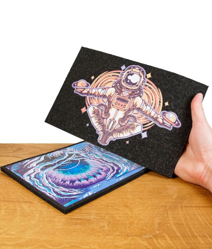Zwei Dab-Mats, übereinandergelegt, mit Astronauten- und Augen-Motiven, auf Holzuntergrund.