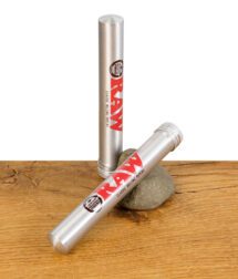 Zwei RAW Aluminium Tubes, eine stehend und eine liegend mit Schraubverschluss, auf Holztisch mit Stein.