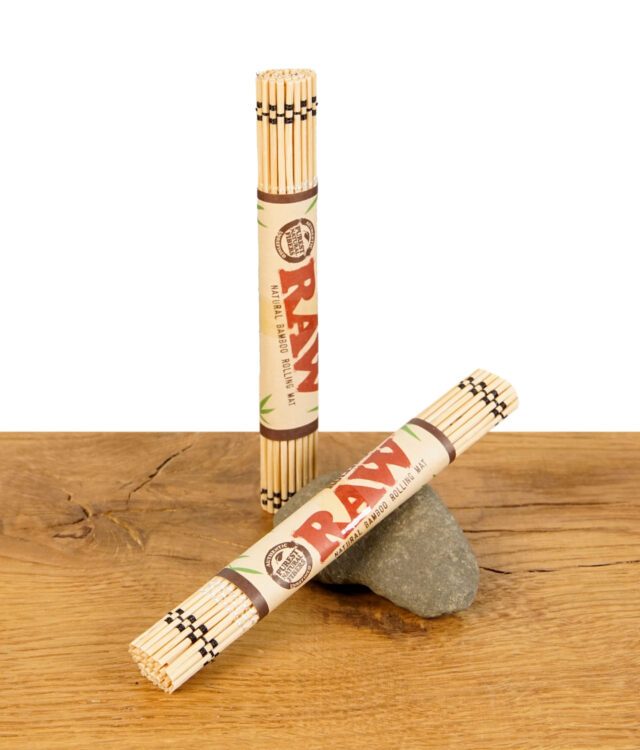 RAW Bamboo Rolling Mat, zusammengerollt und mit Papierbanderole, stehend und liegend auf Holztisch mit Stein.