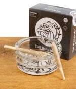 The Bulldog Amsterdam Glas-Aschenbecher mit zwei vorgedrehten Joints, Verpackung im Hintergrund, auf Holztisch.