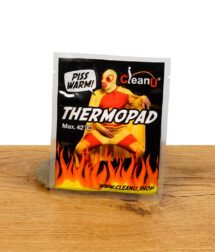 Verpackung des CleanU Thermopads mit auffälligem Design, maximaler Temperatur von 42 °C und einem Feuer-Motiv, auf einem Holztisch präsentiert.