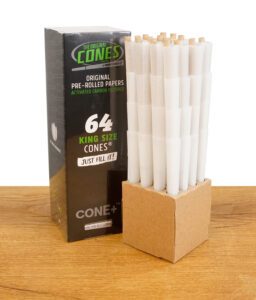 Verpackung der "The Original Cones" King Size mit 64 vorgedrehten Filterhülsen und aktivierter Kohlefilterung, zusammen mit der gestapelten Halterung auf einem Holztisch.