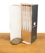 Offene Verpackung der "The Original Cones" King Size, mit vorgedrehten Filterhülsen ordentlich gestapelt, auf einem Holztisch neben einem Stein präsentiert.