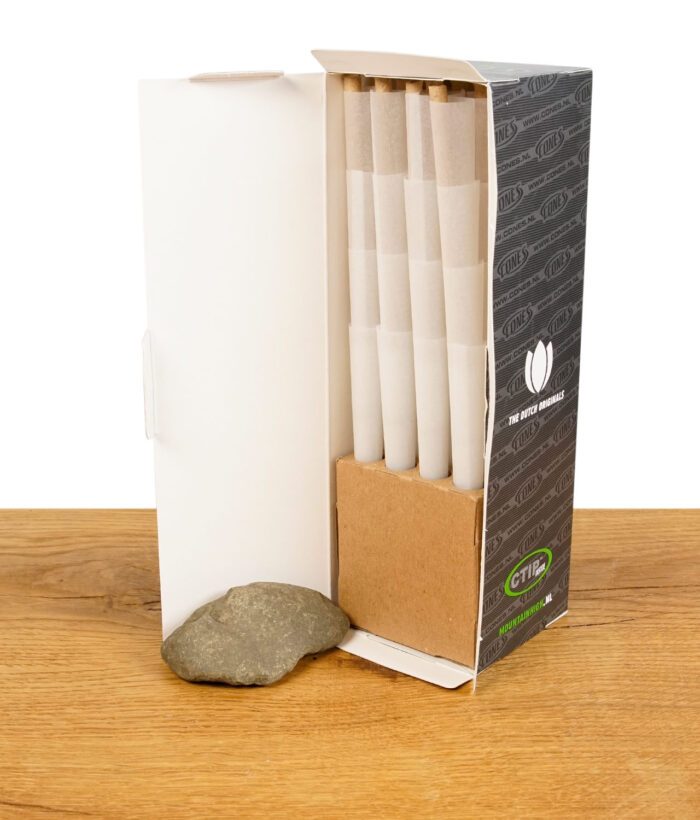Offene Verpackung der "The Original Cones" King Size, mit vorgedrehten Filterhülsen ordentlich gestapelt, auf einem Holztisch neben einem Stein präsentiert.