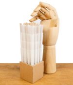 Stapel der vorgedrehten Filterhülsen aus der "The Original Cones" King Size Packung, präsentiert in einer Halterung neben einer Holzhand, auf einem Holztisch.