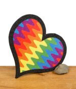 Herzförmiger Dab-Mat mit Regenbogendesign, aufrecht auf Holzuntergrund mit Stein abgestützt.