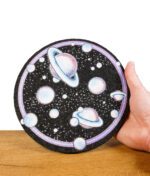 Hand hält runden Dab-Mat mit detailliertem Planeten- und Weltraummotiv.