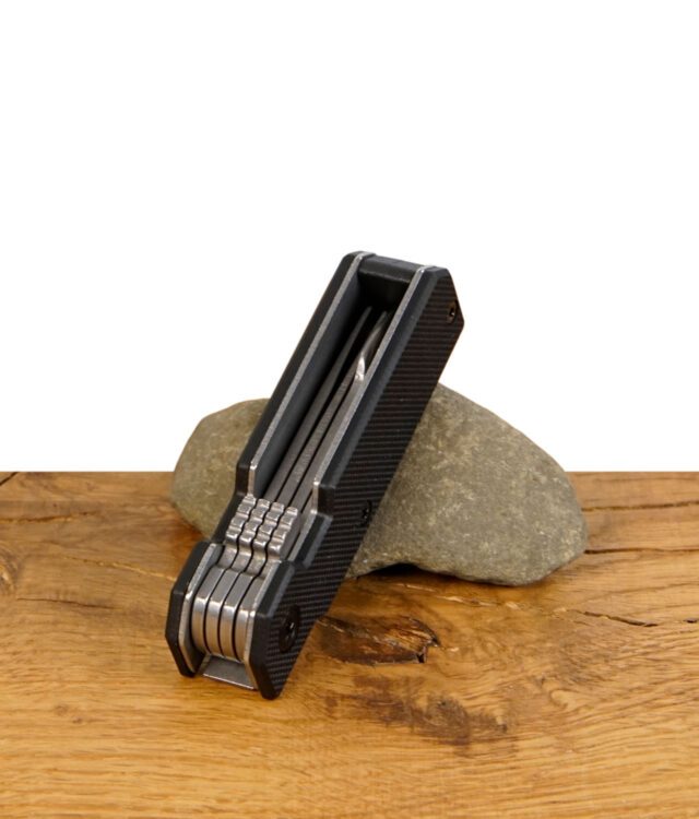 Zusammengeklapptes Everyday Canna Co. Multipass Cannabis-Tool mit mehreren Metallwerkzeugen, liegend auf einem Stein.