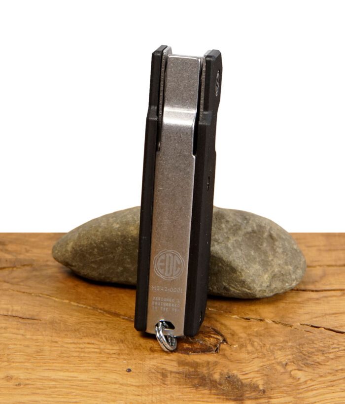 Rückseite des Everyday Canna Co. Multipass Cannabis-Tools mit EDC-Logo und Gravur „Designed & Engineered in the USA“, stehend auf einem Stein.