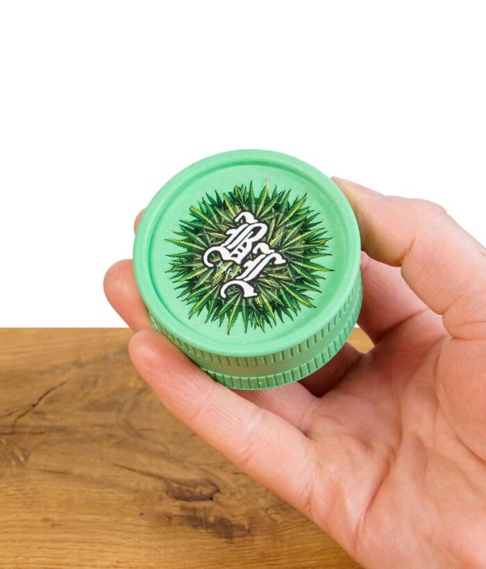 Grüner Hanffaser-Grinder mit Cannabis-Design, in einer Hand gehalten.