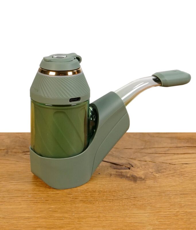 Puffco Proxy mit grünem Silikonständer und Glasmundstück auf Holzuntergrund.