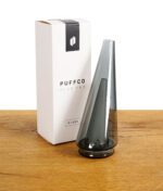 Schwarzer Puffco Peak Pro Glasaufsatz neben der Originalverpackung.