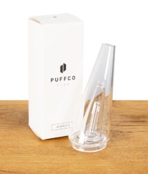 Klarer Puffco Peak Glasaufsatz neben der Originalverpackung auf Holztisch.