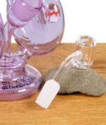 Nahaufnahme eines Glaskopfes mit abgeschrägtem Adapter neben der lila Heady Glass Recycler-Bong.