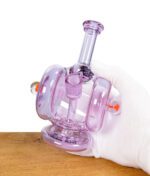Eine Hand mit weißem Handschuh hält die lila Heady Glass Recycler-Bong vorsichtig.