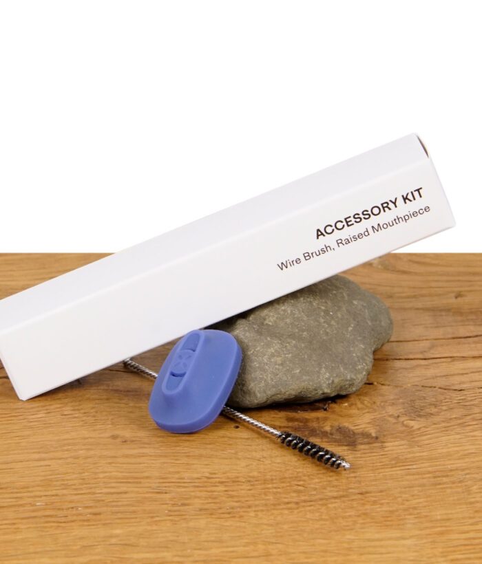 PAX Accessory Kit mit Reinigungsbürste und erhöhtem Mundstück auf Stein platziert.