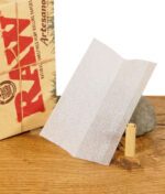 Einzelnes RAW Artesano Organic Hemp Blättchen und ein Filtertip auf einem Stein vor der Verpackung.
