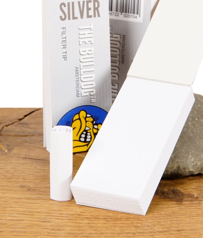 Einzelner gerollter The Bulldog Silver Filter Tip vor einem Stapel ungefalteter Filtertips.