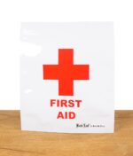 Ein Black Leaf Zipperbeutel mit „First Aid“-Aufdruck und rotem Kreuz steht auf einer Holzoberfläche.