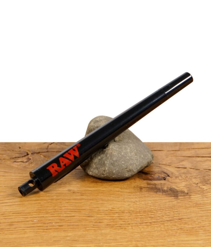 Schwarzes RAW-Metallrohr mit rotem Logo liegt schräg auf einem Stein auf Holzuntergrund.