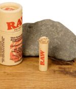 Nahaufnahme des RAW Rose Tips – vorgerollter Filter mit detailreicher Rosenspitze, stehend vor der RAW-Verpackung auf Holzoberfläche.