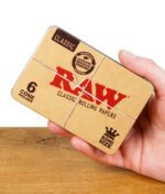 RAW Classic Cone Holder Metalldose in einer Hand gehalten, zeigt das authentische RAW-Design mit Schnurmotiv.