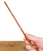 RAW Wooden Poker – naturbelassener Holztamper mit RAW-Logo, gehalten zwischen Daumen und Finger vor Holztisch-Hintergrund.
