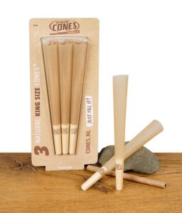 Packung mit drei ungebleichten The Original Cones King Size – vorgedrehte Cones aus Naturpapier, präsentiert auf Holztisch mit Stein.