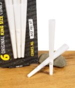 Nahaufnahme der The Original King Size Cones Packung mit sechs vorgedrehten Cones, daneben lose Cones auf Holztisch mit Stein.