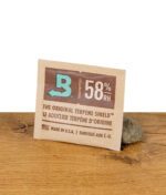 Boveda 58% Feuchtigkeitspack – Terpene Shield zur Feuchtigkeitskontrolle bei der Lagerung von Kräutern, präsentiert auf Holztisch mit Stein.