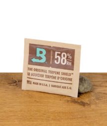 Boveda 58% Feuchtigkeitspack – Terpene Shield zur Feuchtigkeitskontrolle bei der Lagerung von Kräutern, präsentiert auf Holztisch mit Stein.