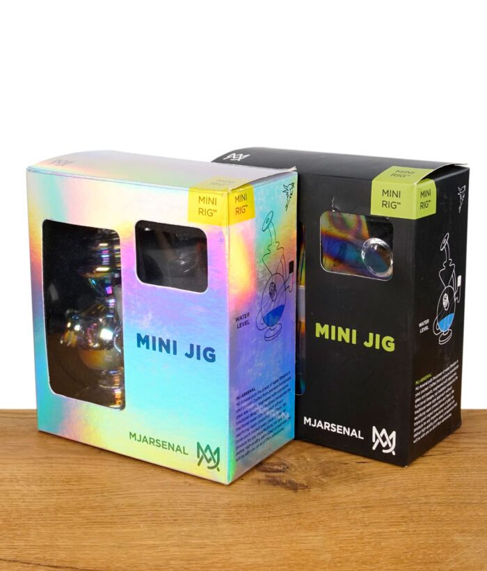 Verpackung des MJ Arsenal Mini Jig Dab Rigs in zwei Farbvarianten – holografisch und schwarz, präsentiert auf Holztisch.
