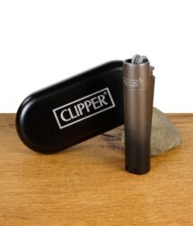 Clipper Metall-Feuerzeug in Gunmetal mit schwarzem Etui auf einem Holztisch.