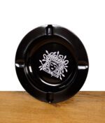 Schwarzer Aschenbecher mit weißem Medusa-Design auf Holzuntergrund.
