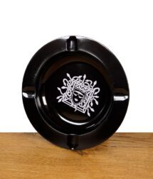 Schwarzer Aschenbecher mit weißem Medusa-Design auf Holzuntergrund.